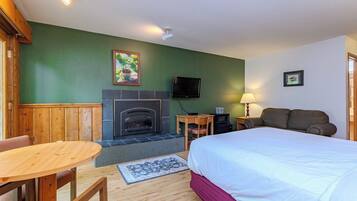 A hotel room with a bed, a small table, a chair, a fireplace, a TV, and a lamp.