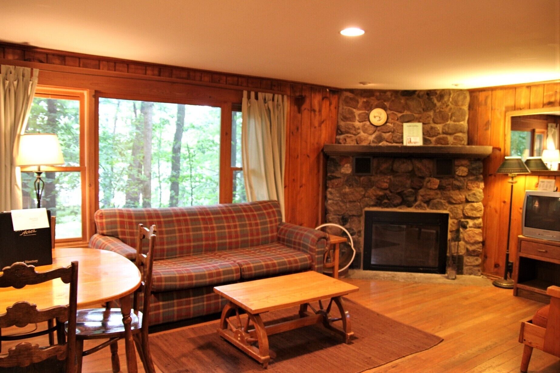 A cozy living room with a plaid sofa, a fireplace, a stone wall, and wooden floors.