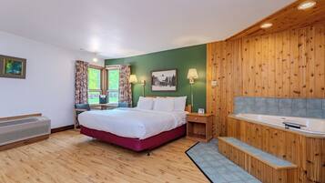 A hotel room with a bed, a desk, a chair, a window with curtains, a painting, a lamp, a wooden wall paneling, and a bathtub.
