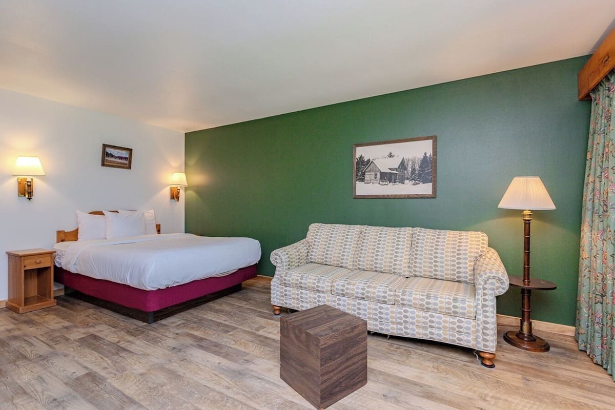 A bedroom with a bed, a wooden nightstand, a patterned sofa, a small wooden stool, and a lamp.