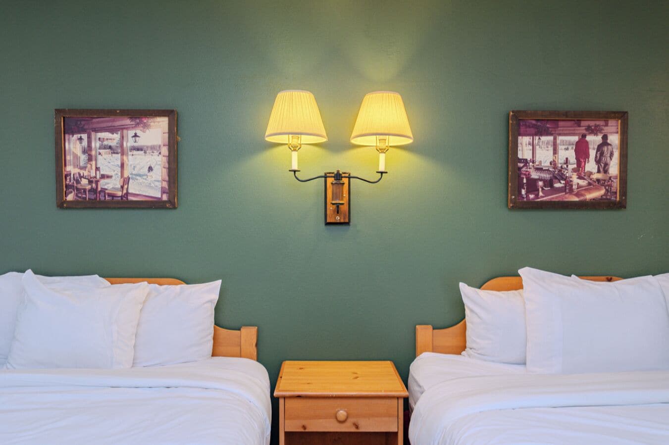 A hotel room with two beds, a nightstand, and wall-mounted lamps.
