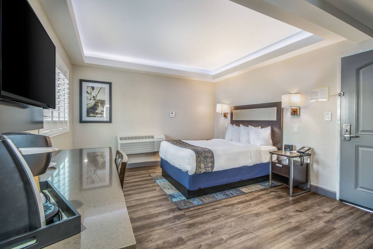 A hotel room with a bed, bedside table, lamp, and a flat-screen TV.