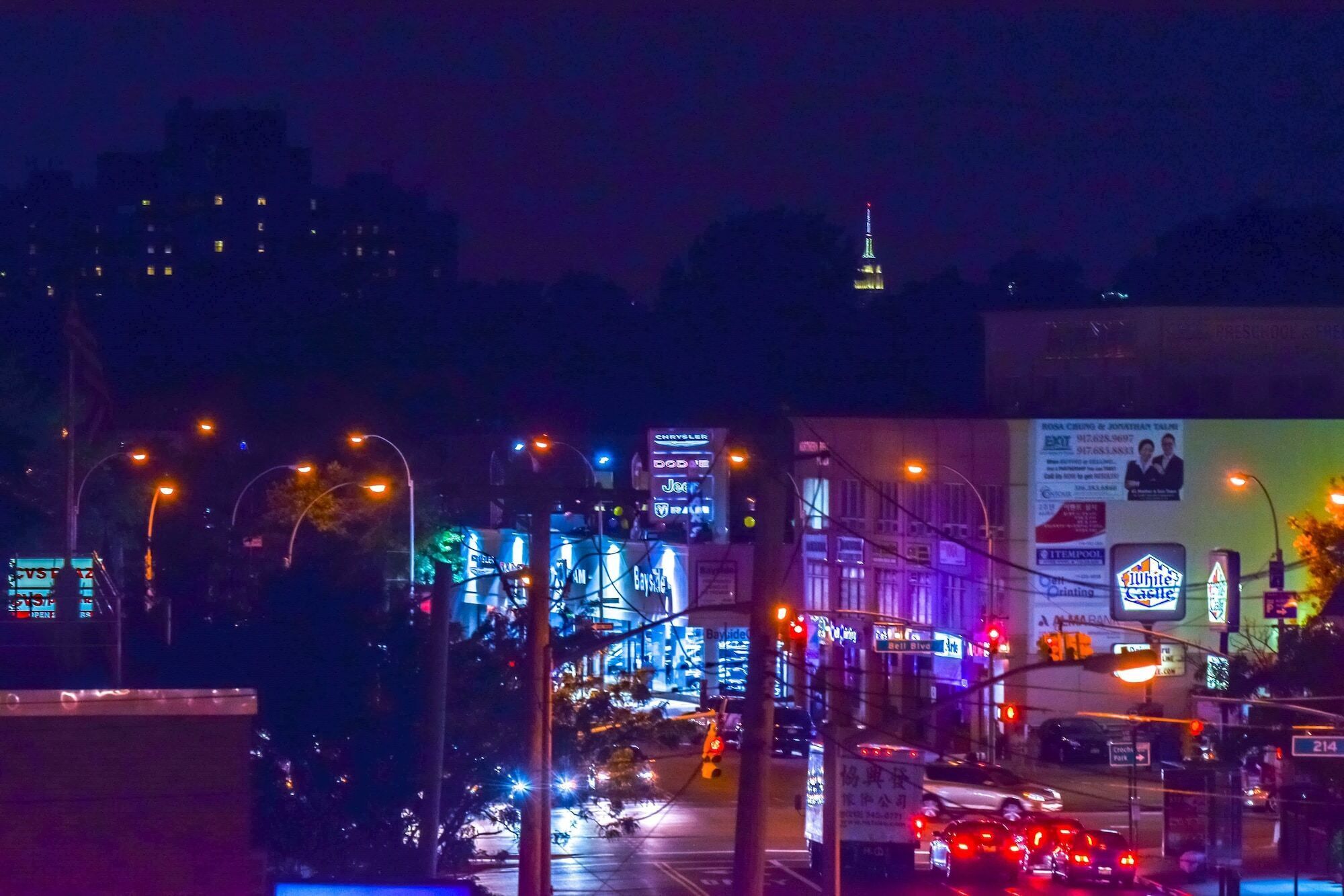 Une rue de la ville de nuit, avec des panneaux publicitaires illuminés et des feux de signalisation.
