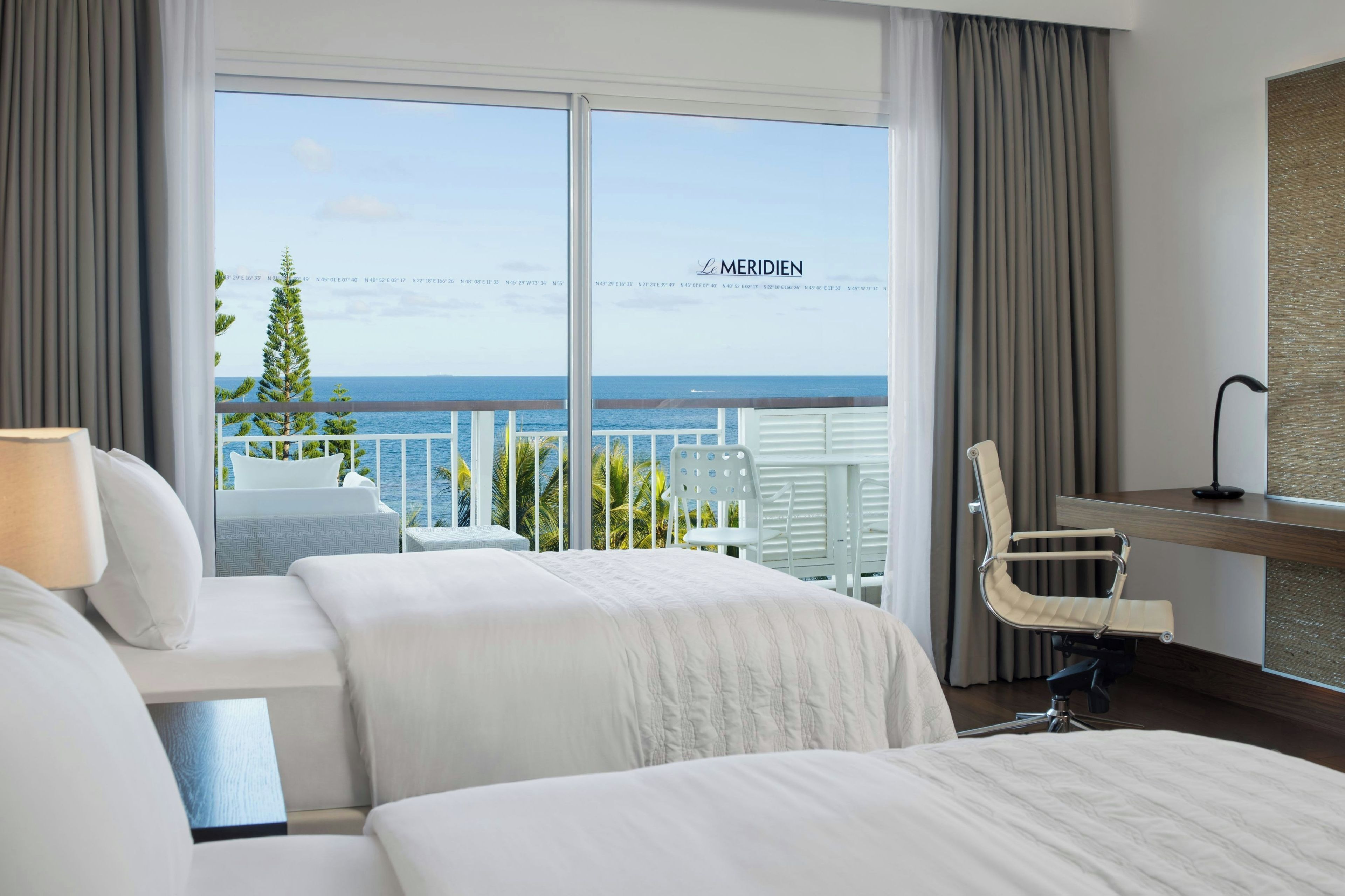Habitación de hotel con dos camas, un escritorio, una silla y vistas al mar.