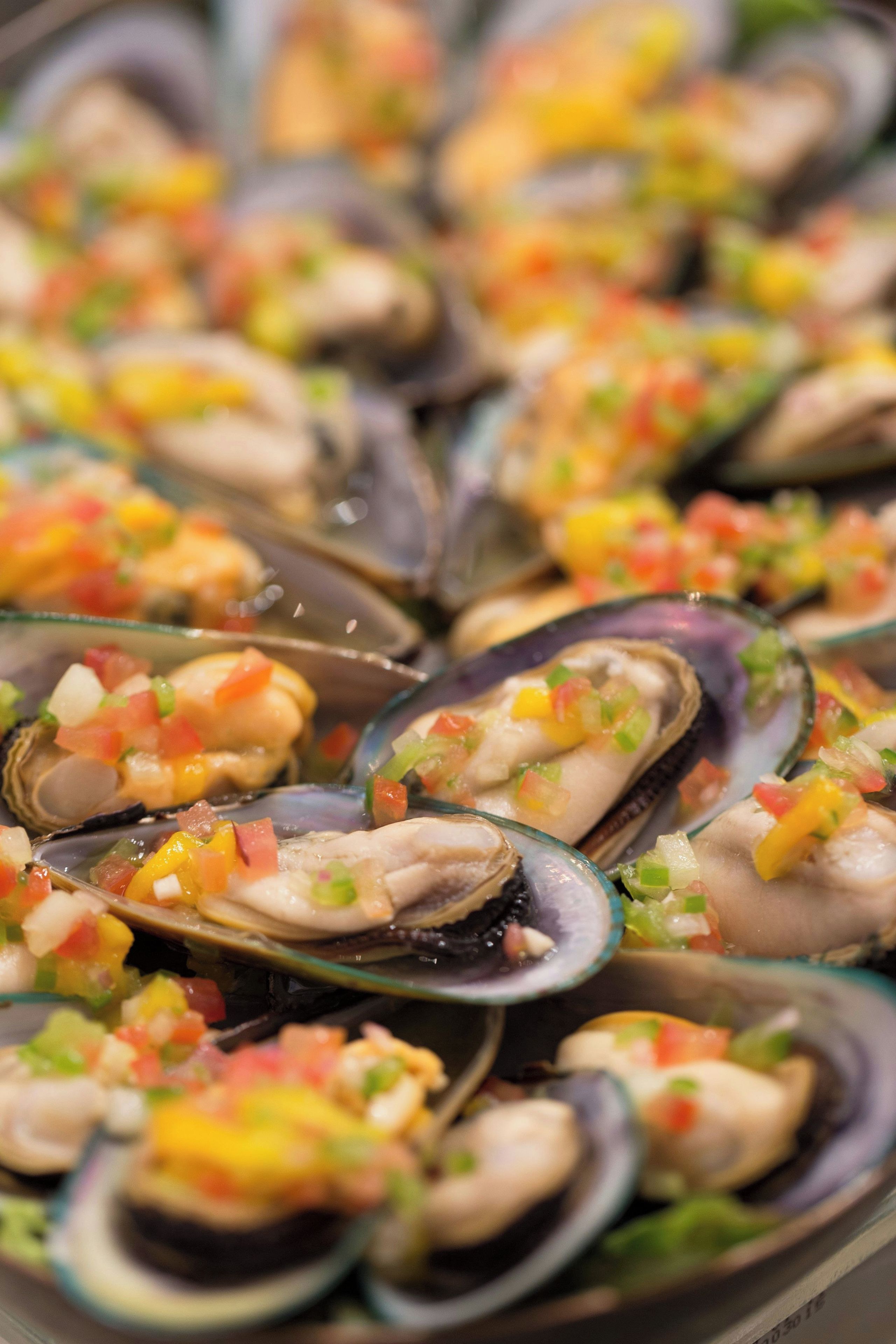 Ein Nahaufnahme eines Fischgerichts mit Muscheln und gewürfelten Gemüsesorten.