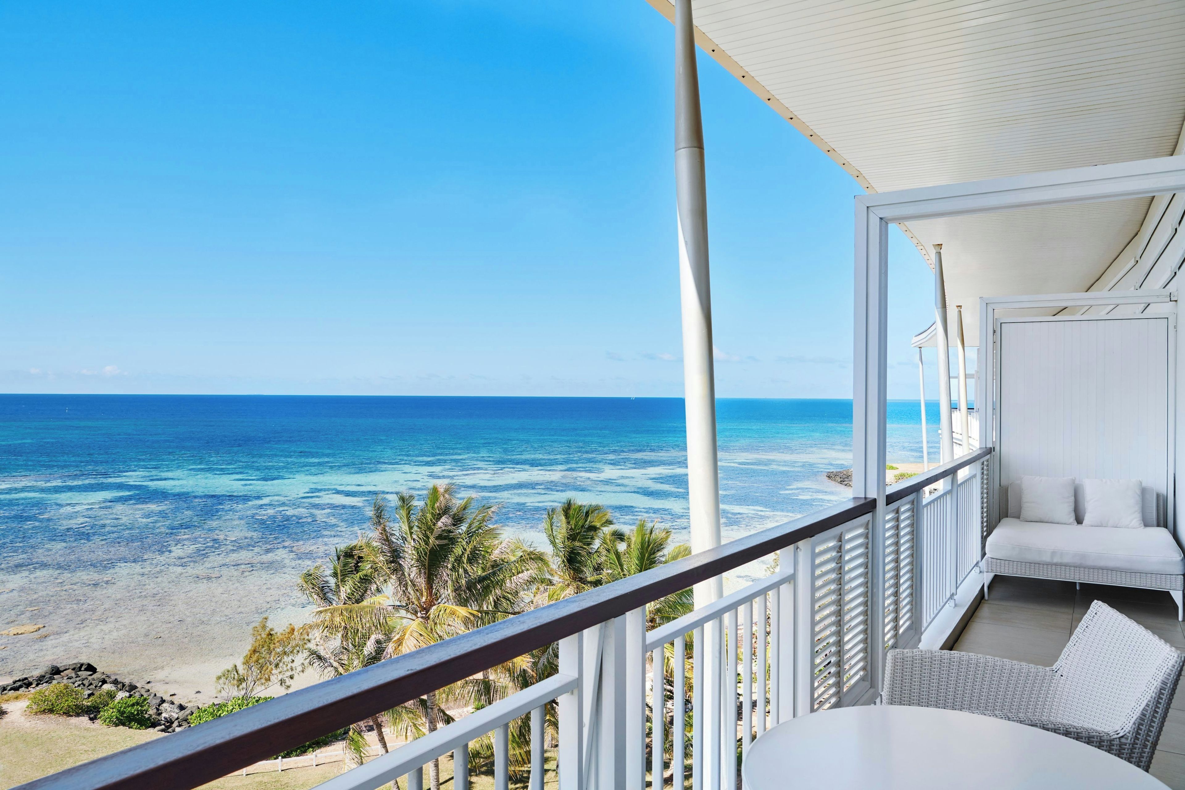 A balcony with a view of the ocean, a white sofa, and a wicker chair.