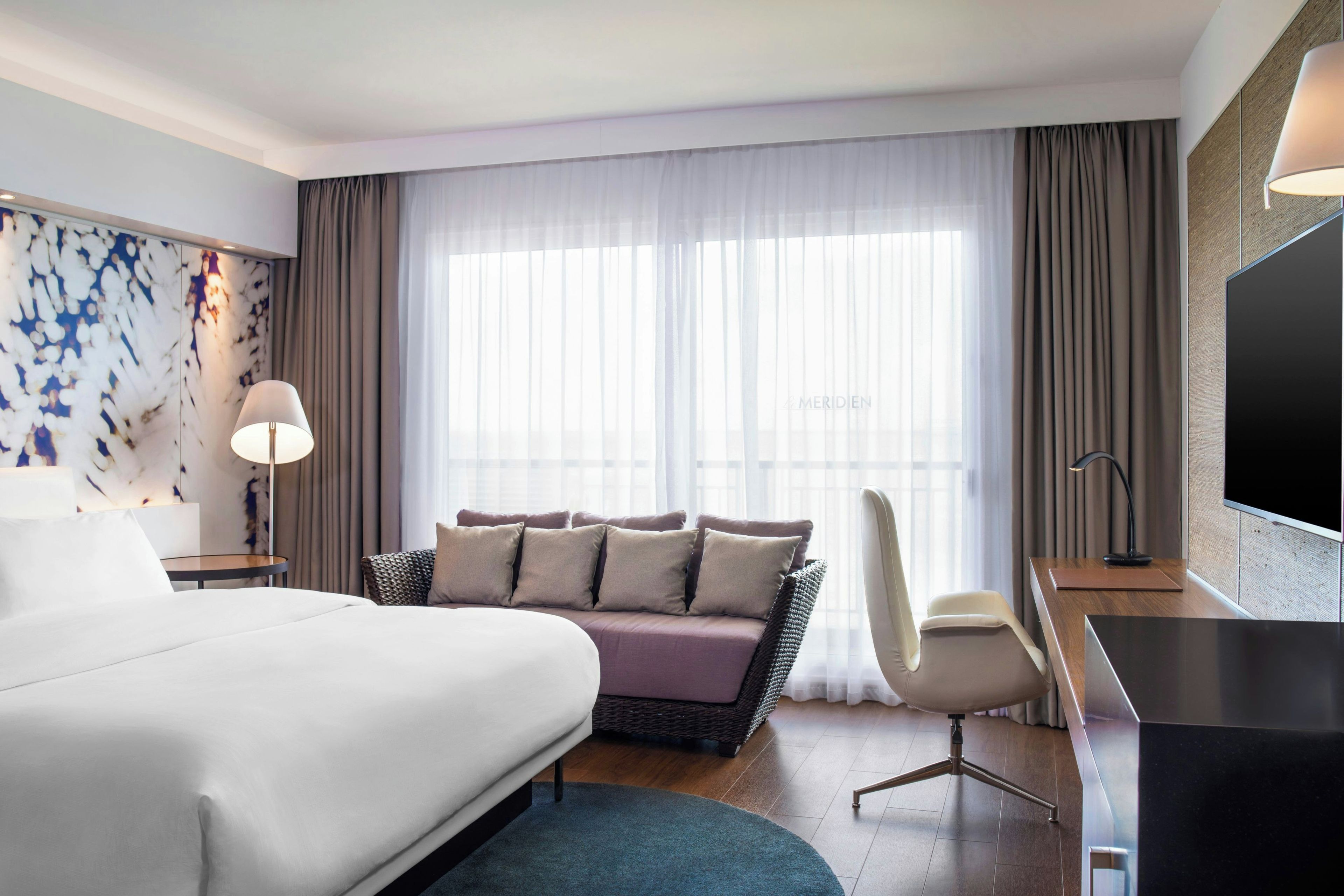 Une chambre d’hôtel avec un grand lit, un canapé, un bureau avec une chaise, une télévision et une fenêtre avec des rideaux.