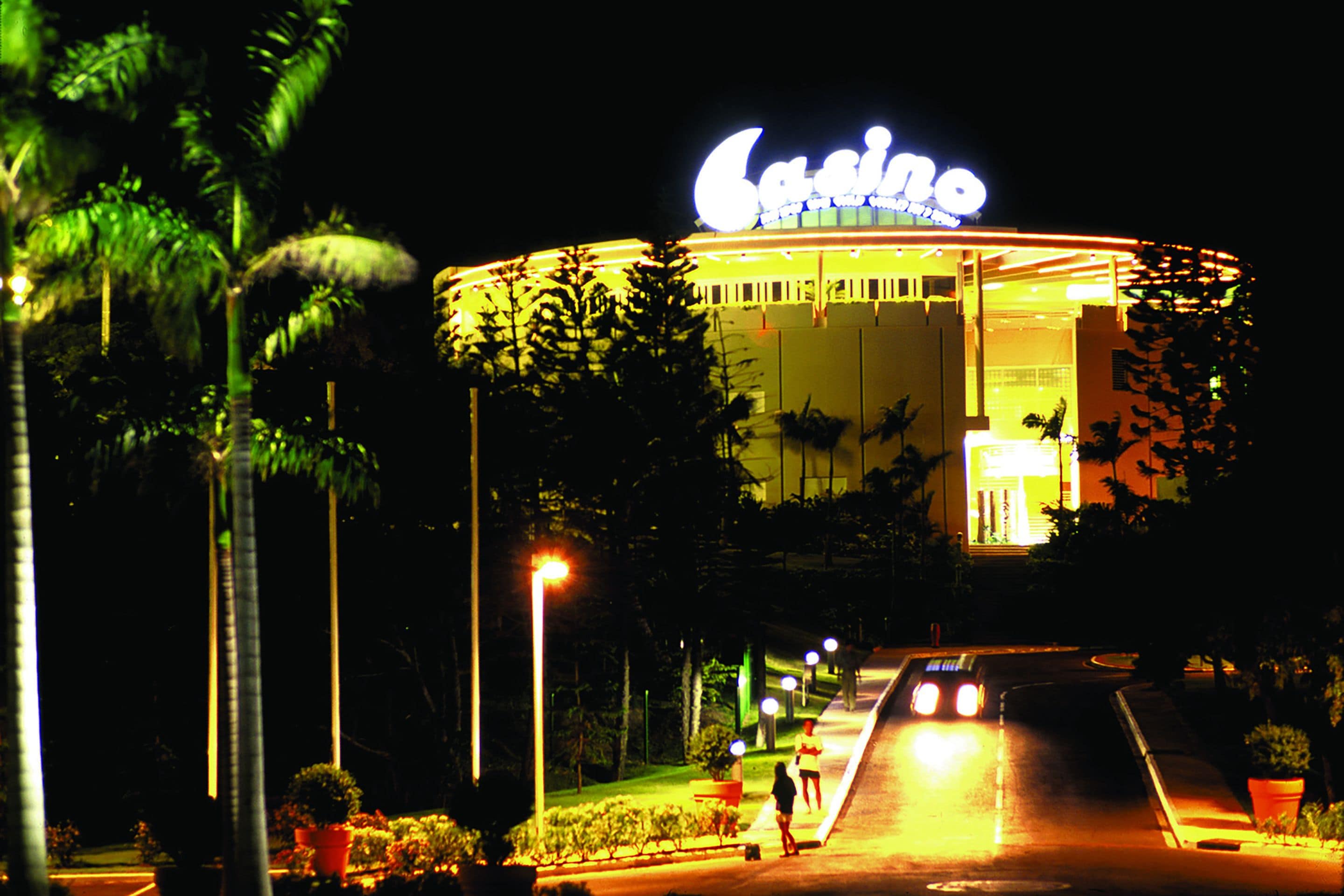 A casino building with a prominent illuminated sign, surrounded by palm trees and street lamps.