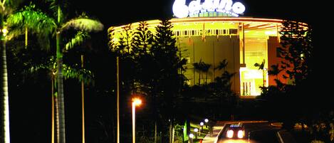 A casino building with a prominent illuminated sign, surrounded by palm trees and street lamps.