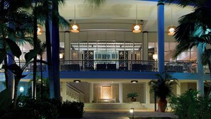 Un hotel a più livelli con un balcone, palme e un ingresso ben illuminato.
