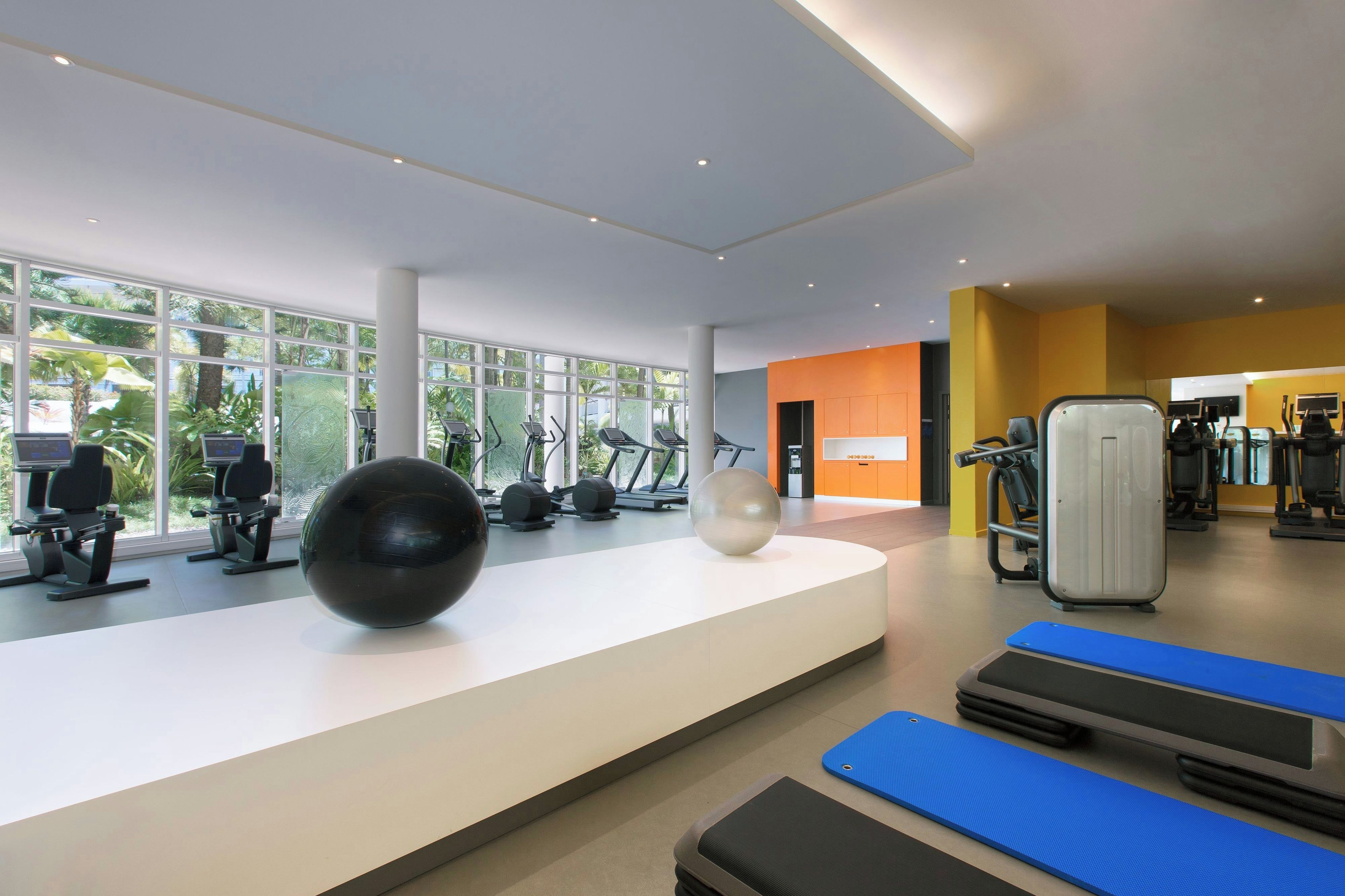 A modern gym with various exercise equipment, large windows, and a bright interior.