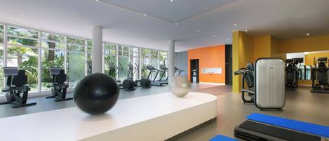 A modern gym with various exercise equipment, large windows, and a bright interior.