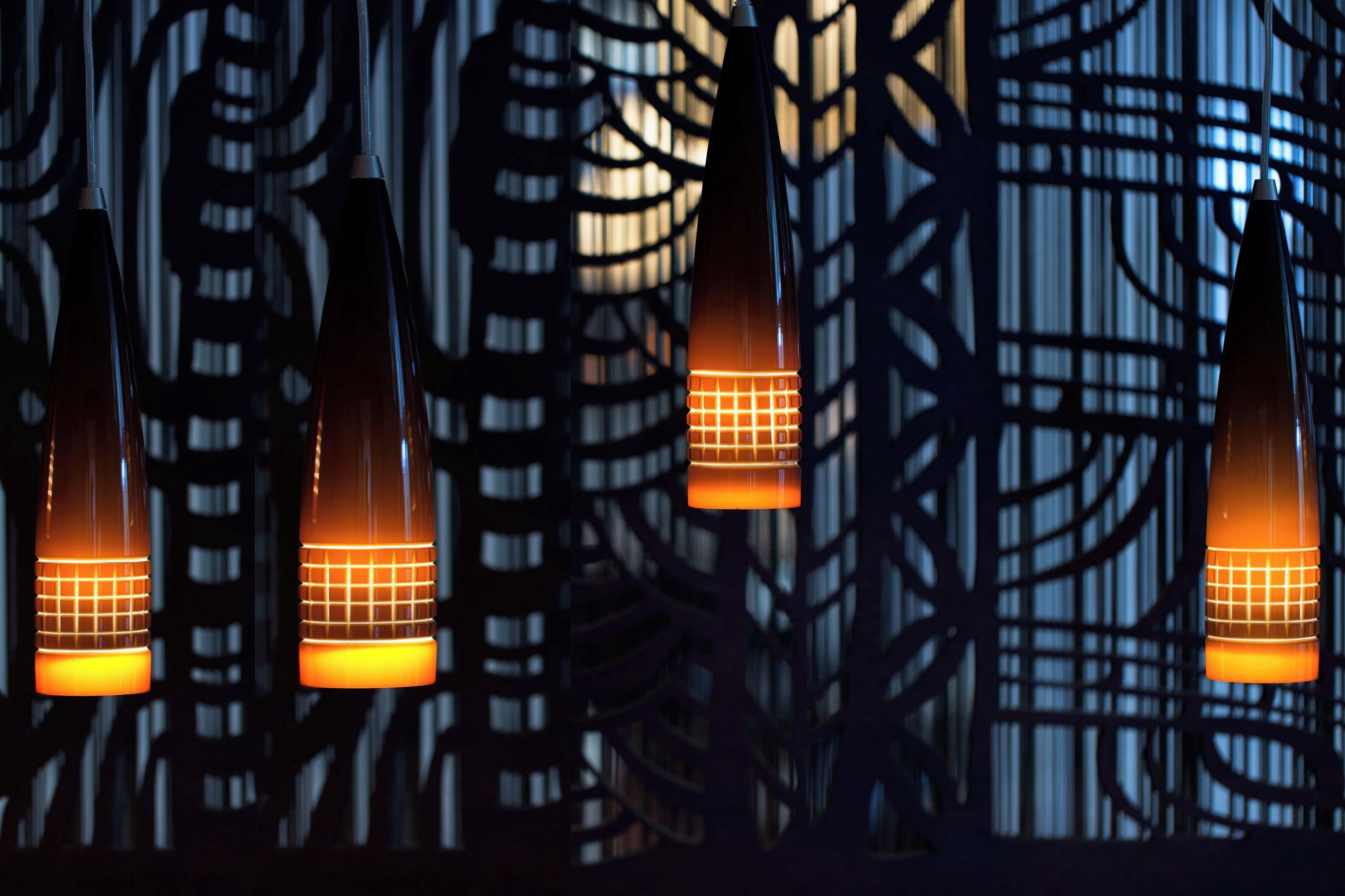 Una serie di lampade a sospensione con motivo a griglia, su sfondo di un edificio con facciata geometrica.