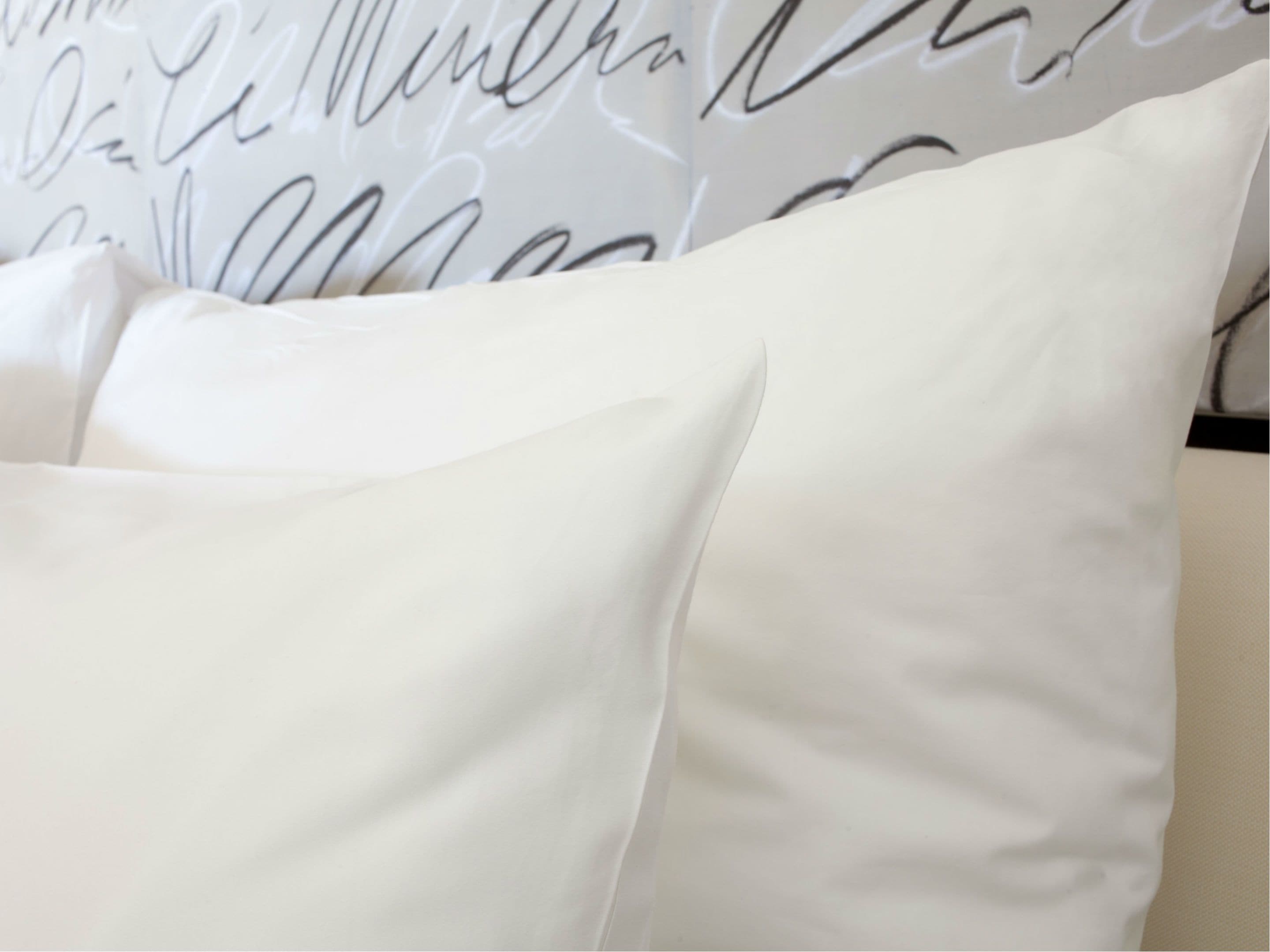 A white pillow with a smooth texture against a wall with cursive writing.