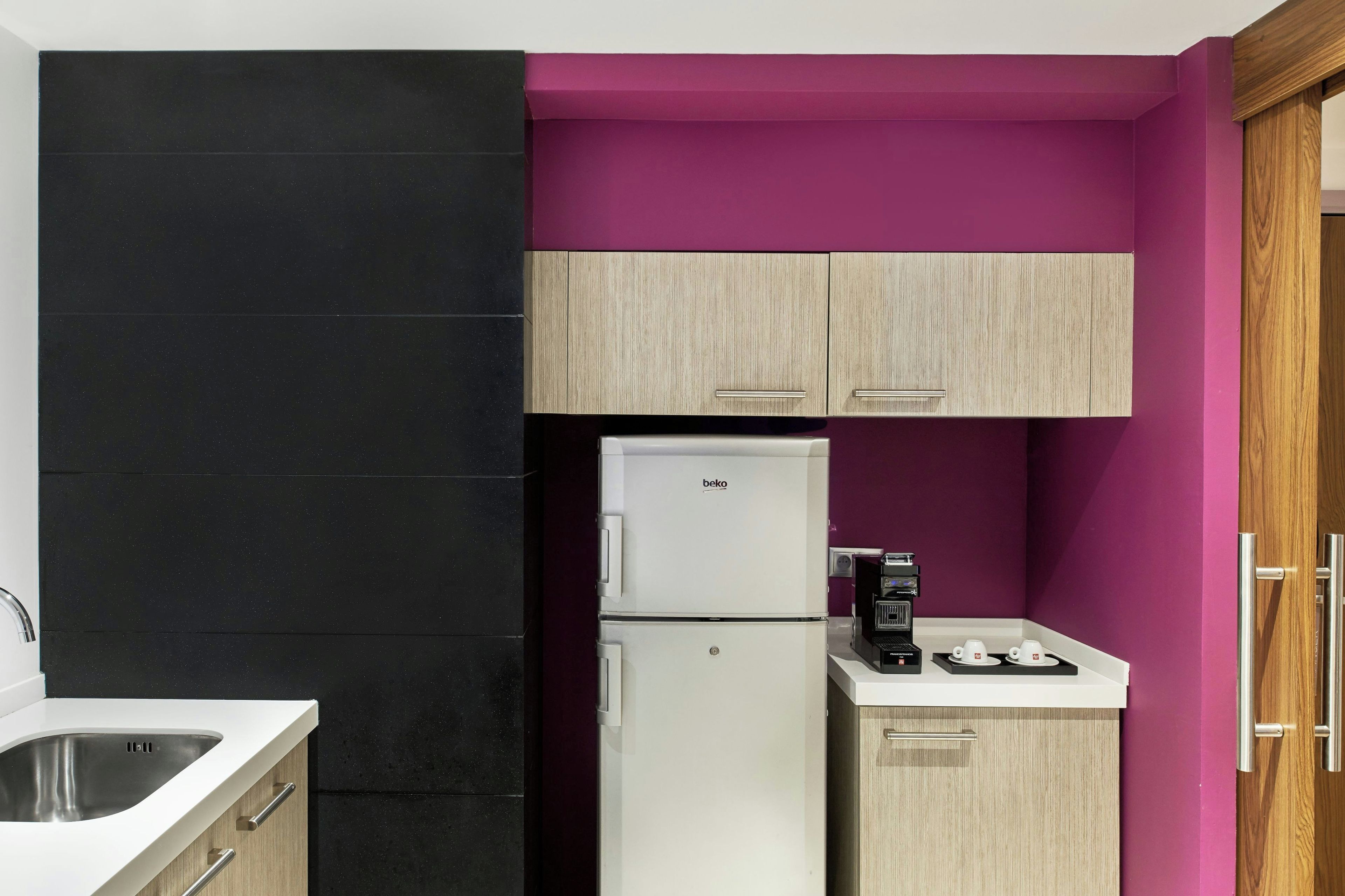A compact kitchen with a white refrigerator, a coffee machine, and a sink.