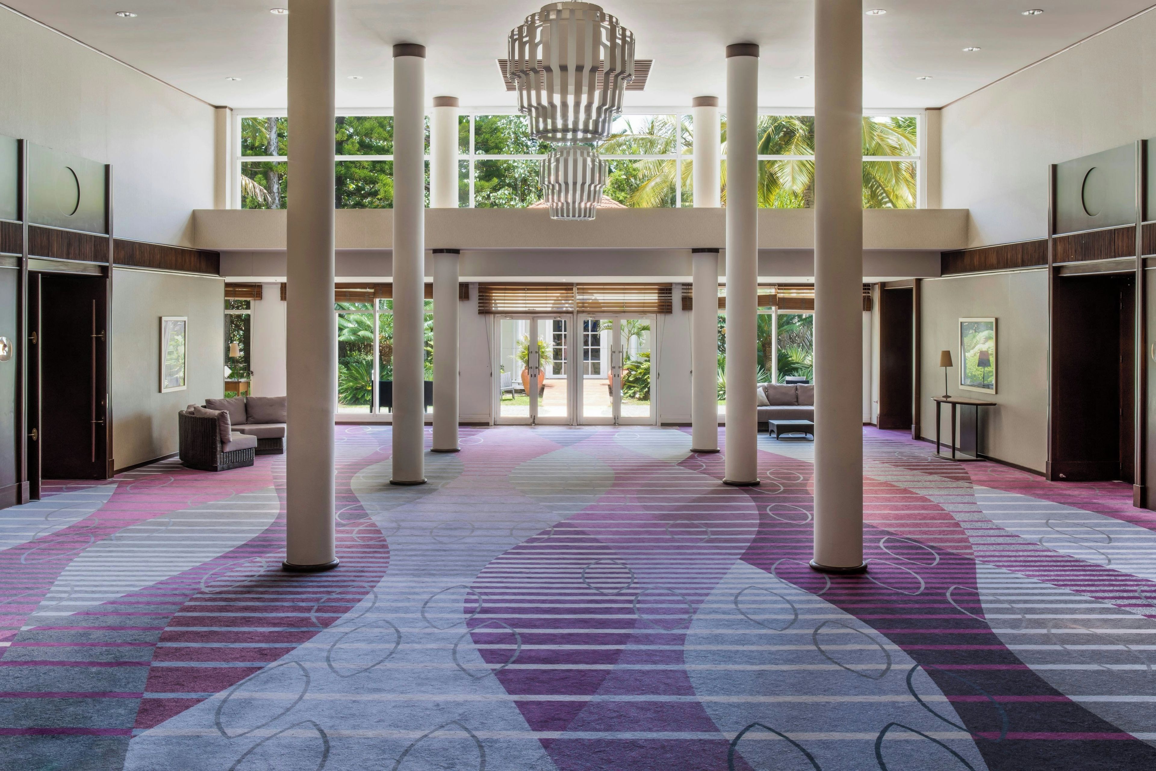 A spacious lobby with a patterned carpet, large columns, and a modern chandelier.
