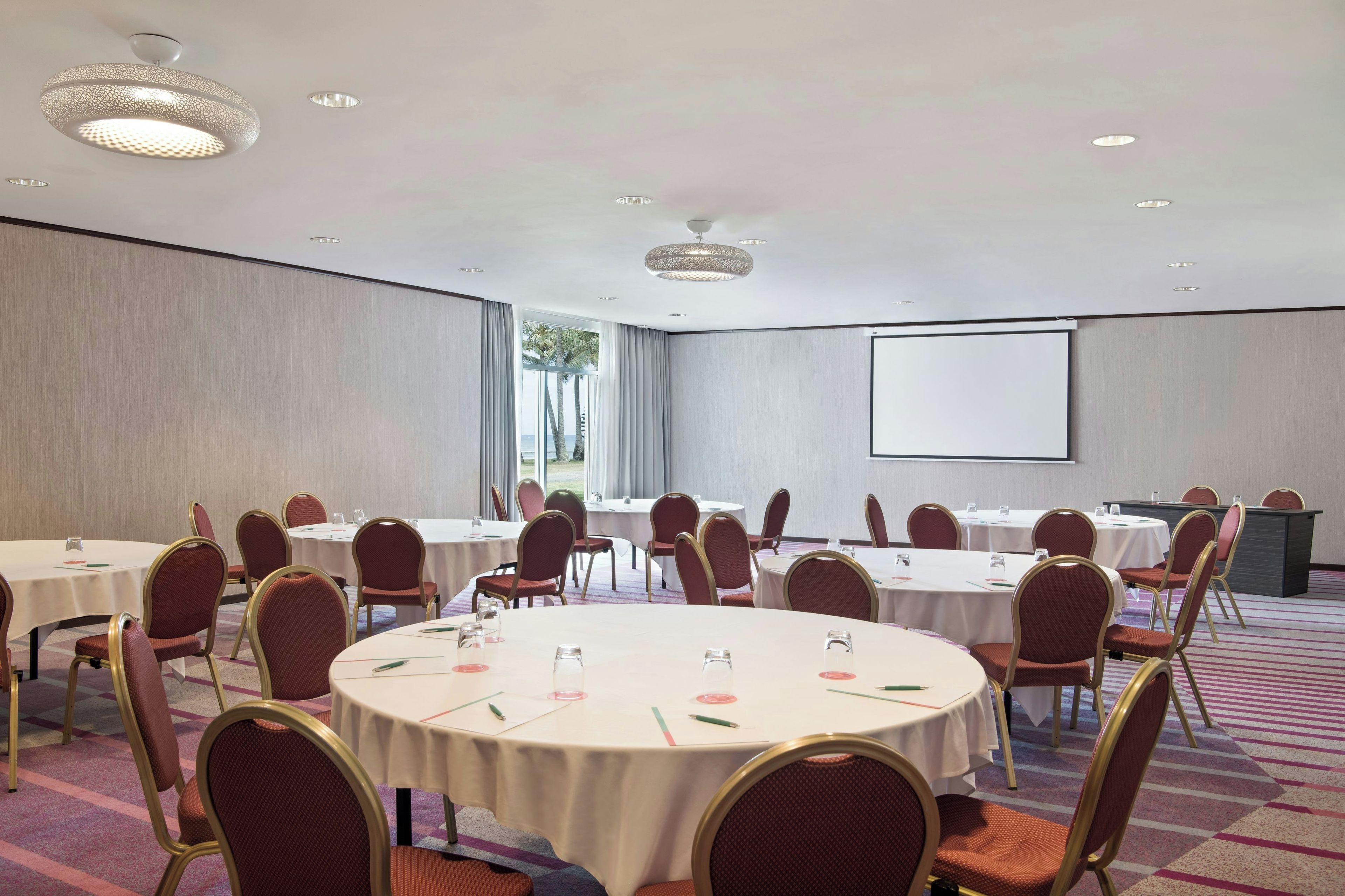A conference room with round tables, chairs, and a projector screen.