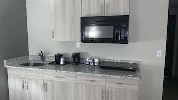 A kitchen with a granite countertop, stainless steel sink, and a black microwave. There are cabinets below and a coffee maker on the counter.