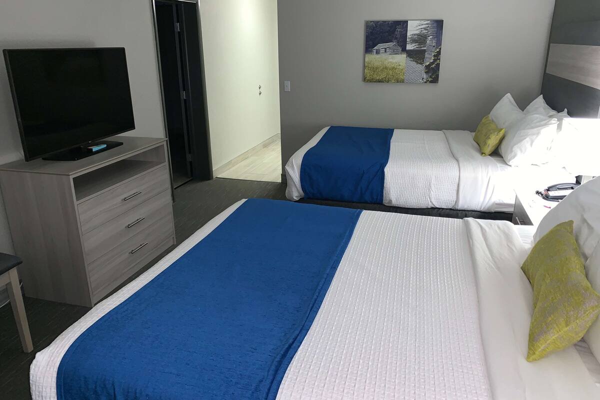 Hotellihuone, jossa on kaksi sänkyä, televisio, työpöytä ja taulu seinällä.