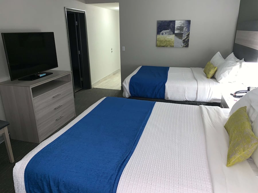 A hotel room with two beds, a TV, a desk, and a painting on the wall.