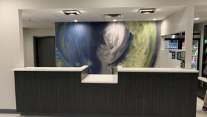 Un mostrador de recepción de diseño moderno, un gran mural abstracto en la pared y un refrigerador lleno de bebidas.