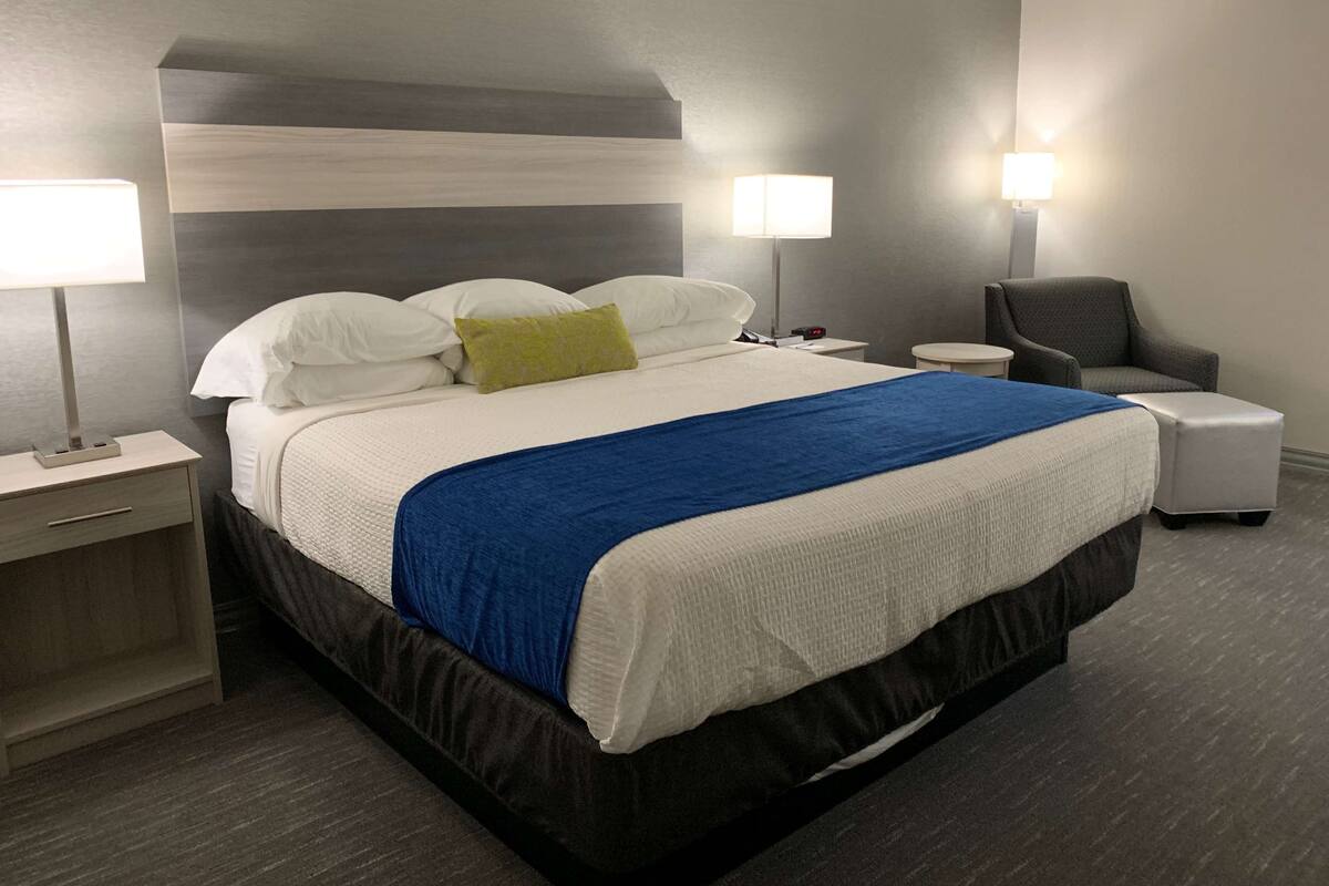Hotellihuone, jossa on suuri sänky, kaksi yöpöytää, tuoli ja pieni sivupöytä.