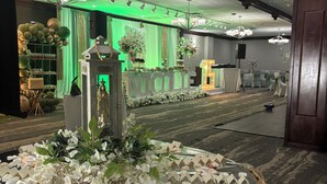 Un área de recepción con una exhibición decorativa de tarjetas con nombres y flores, un fondo iluminado en verde y un candelabro.