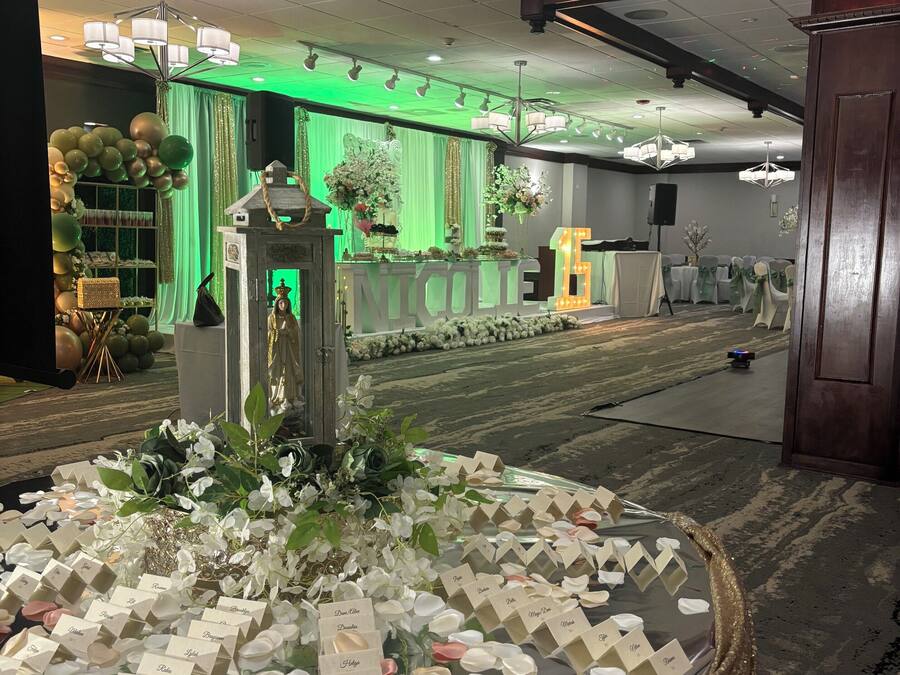 Ein Empfangsbereich mit dekorativer Namensschild- und Blumenpracht, einem grün beleuchteten Hintergrund und einer Kristallleuchter.