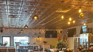 Un restaurante con techo alto, iluminación colgante y un árbol de Navidad. Las mesas están dispuestas con manteles blancos y sillas.