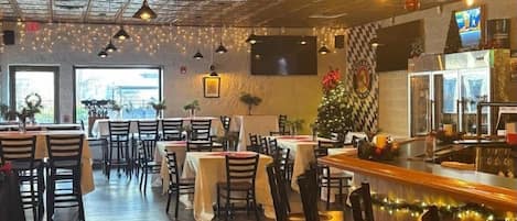 A restaurant with a high ceiling, pendant lighting, and a Christmas tree. Tables are set with white tablecloths and chairs.