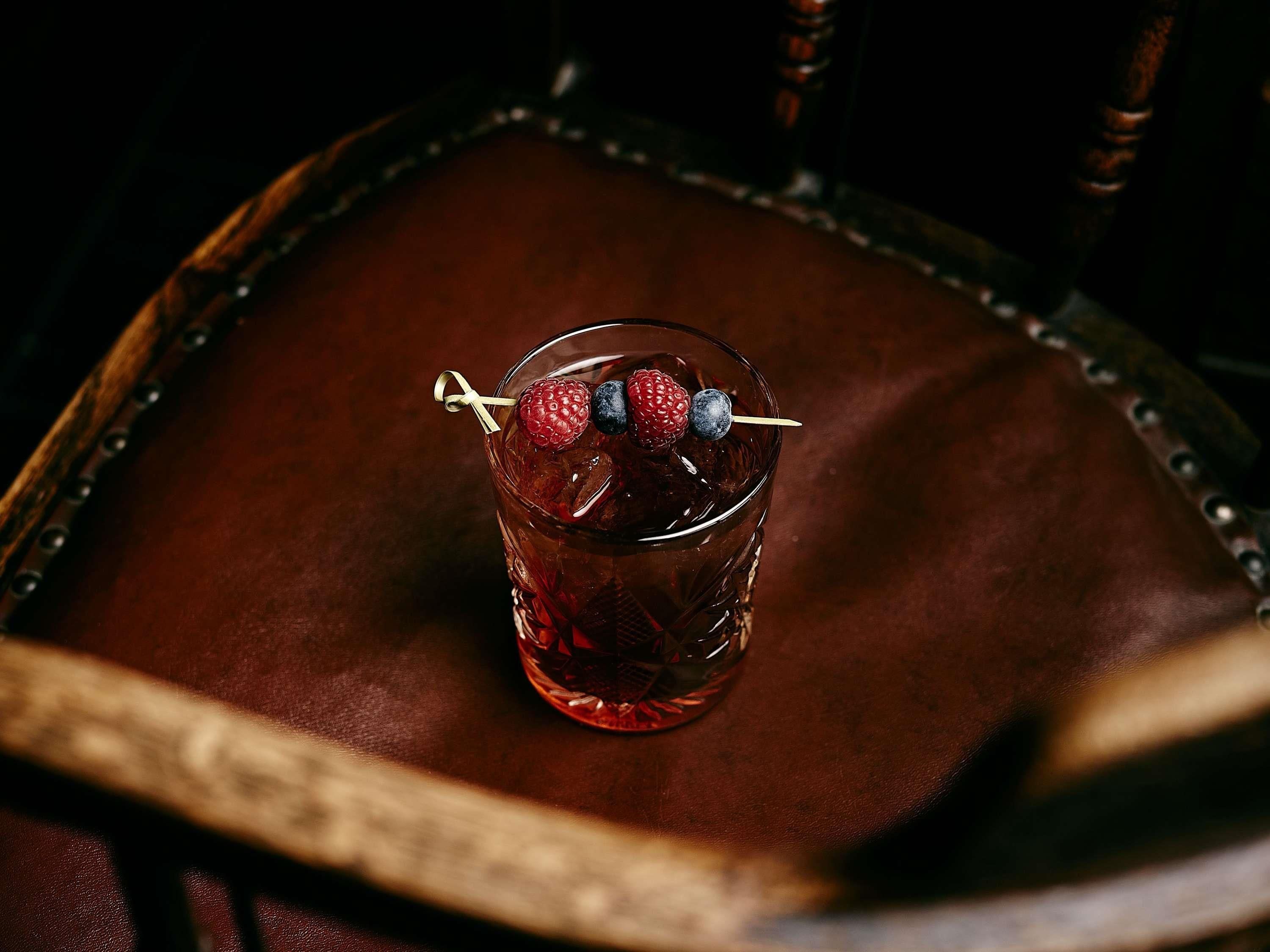 Un vaso de bebida roja con brochetas de frutas sobre una superficie de cuero.