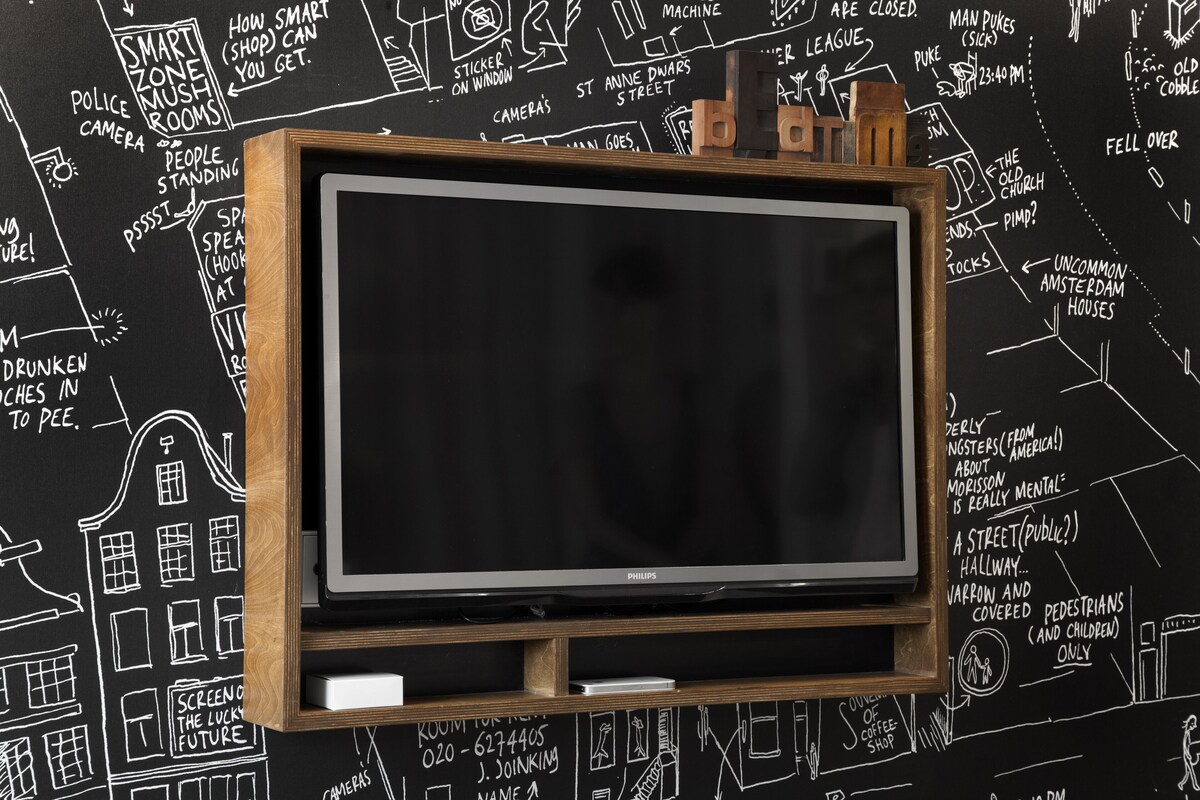 A television set mounted on a wooden frame with a black background featuring white hand-drawn sketches and text.