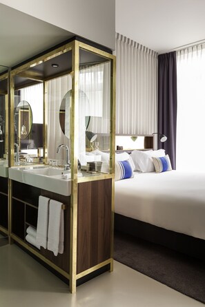 Una habitación de hotel moderna con un amplio tocador de baño, una cama doble y un espejo grande.