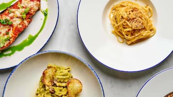 Tres platos de comida: un filete de pescado con salsa, espagueti con queso rallado y pasta verde con acompañamientos fritos.