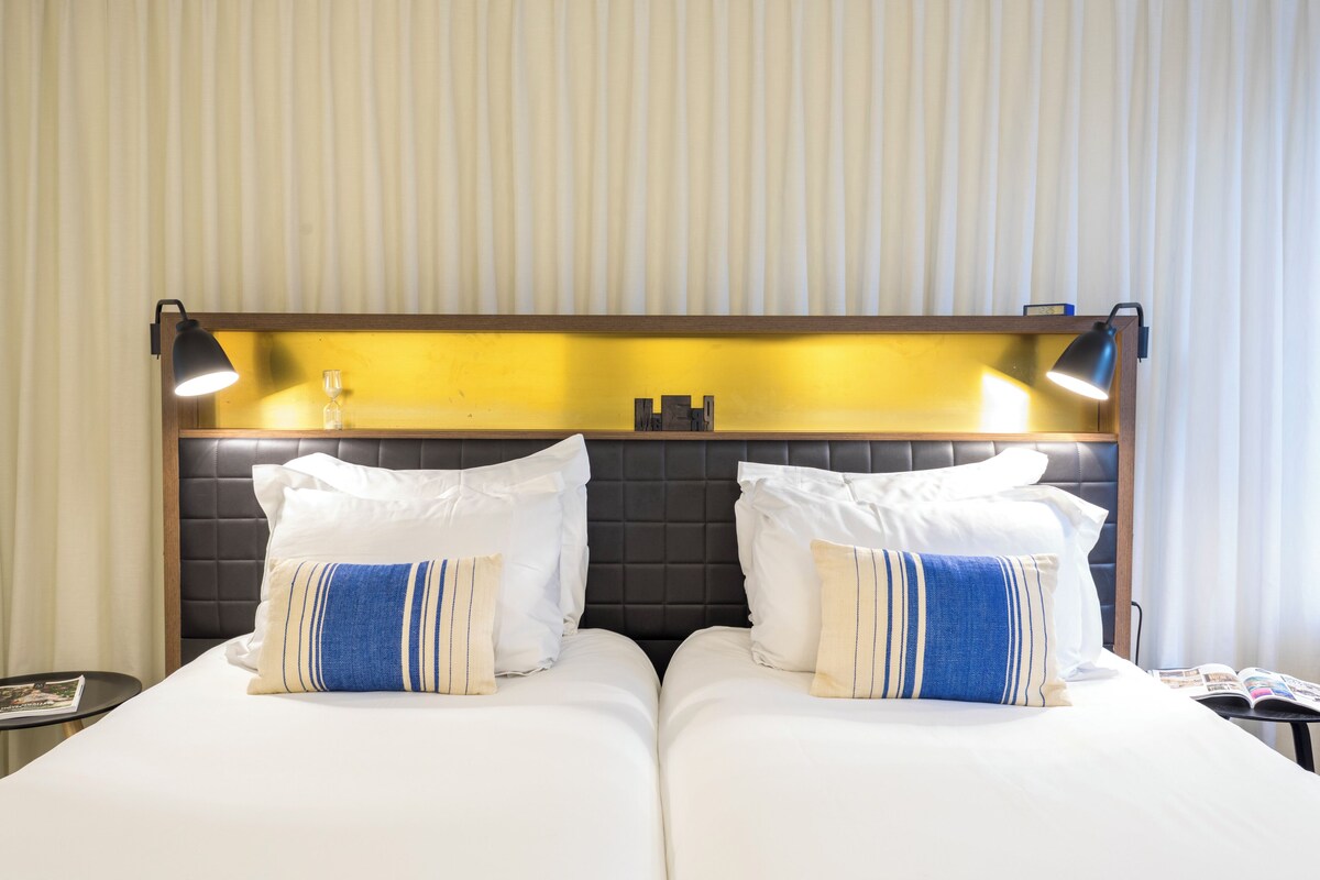 A double bed with white and blue striped pillows, a wooden headboard, and two bedside lamps.