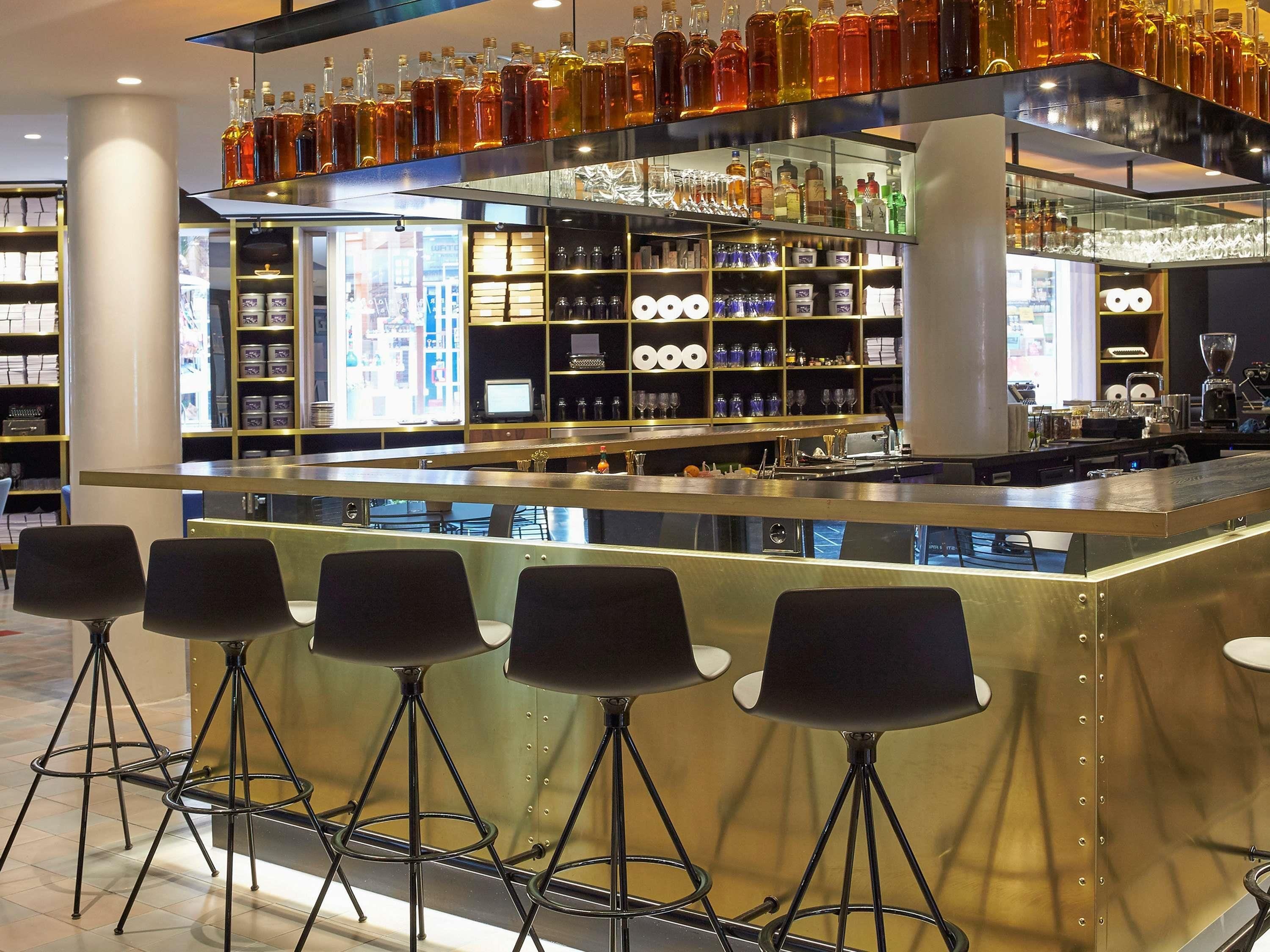 Un área de bar con taburetes, estantes llenos de botellas y un monitor de computadora.