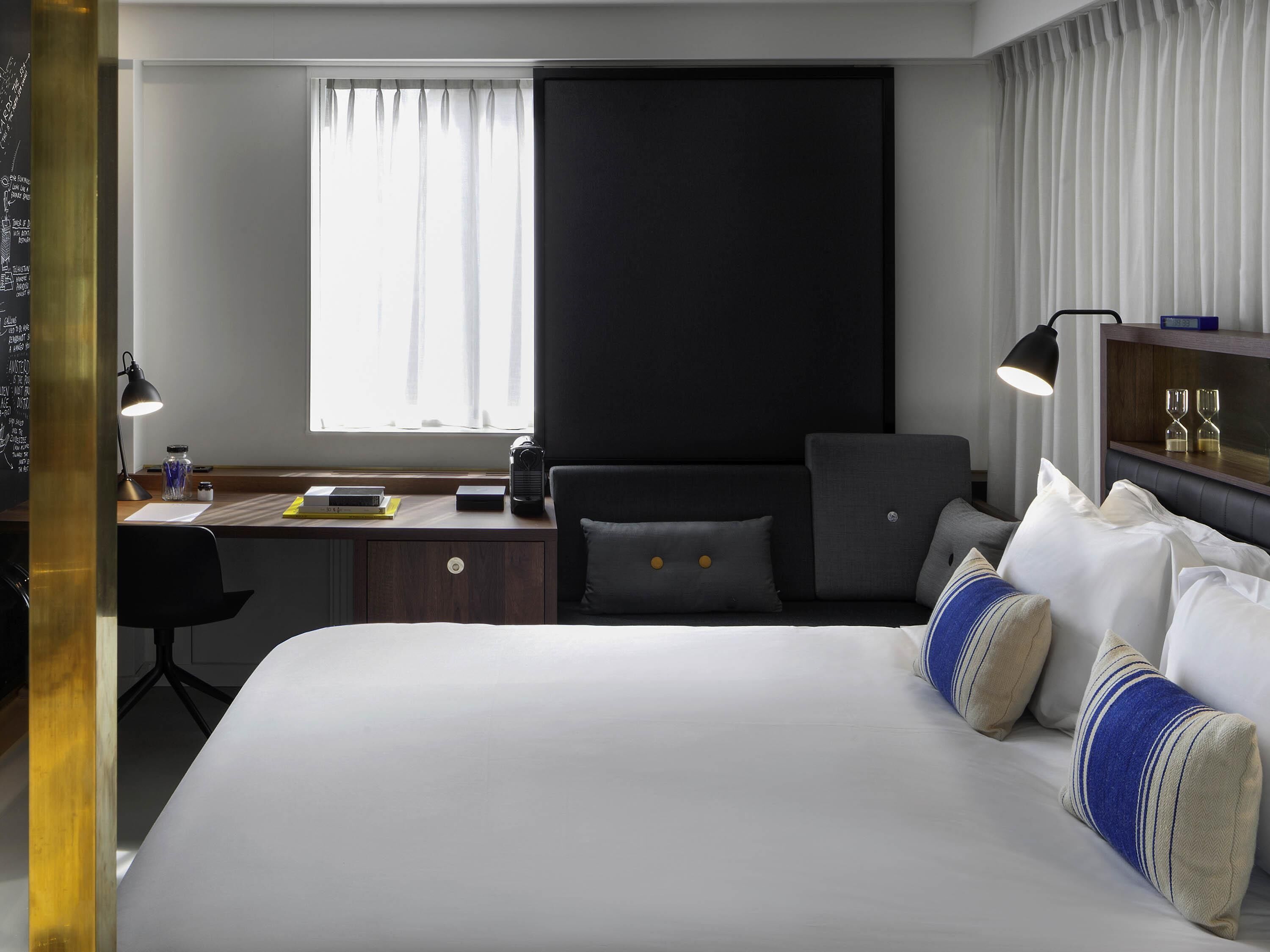 Ein Hotelzimmer mit einem großen Bett, einem Schreibtisch mit Lampe, einem Sessel und einem Fenster mit Vorhängen.