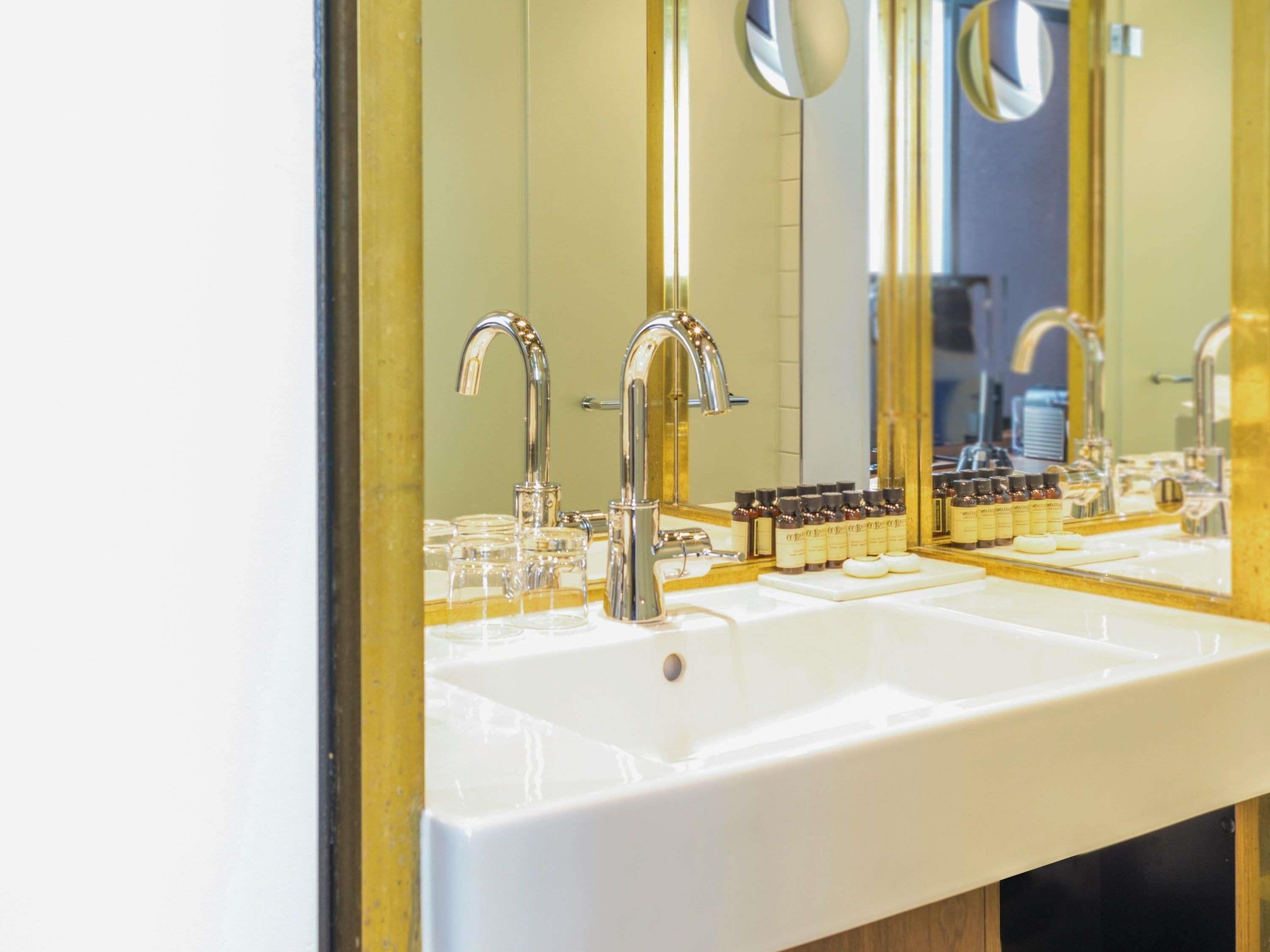 A bathroom with a white sink, two chrome faucets, and a mirror.