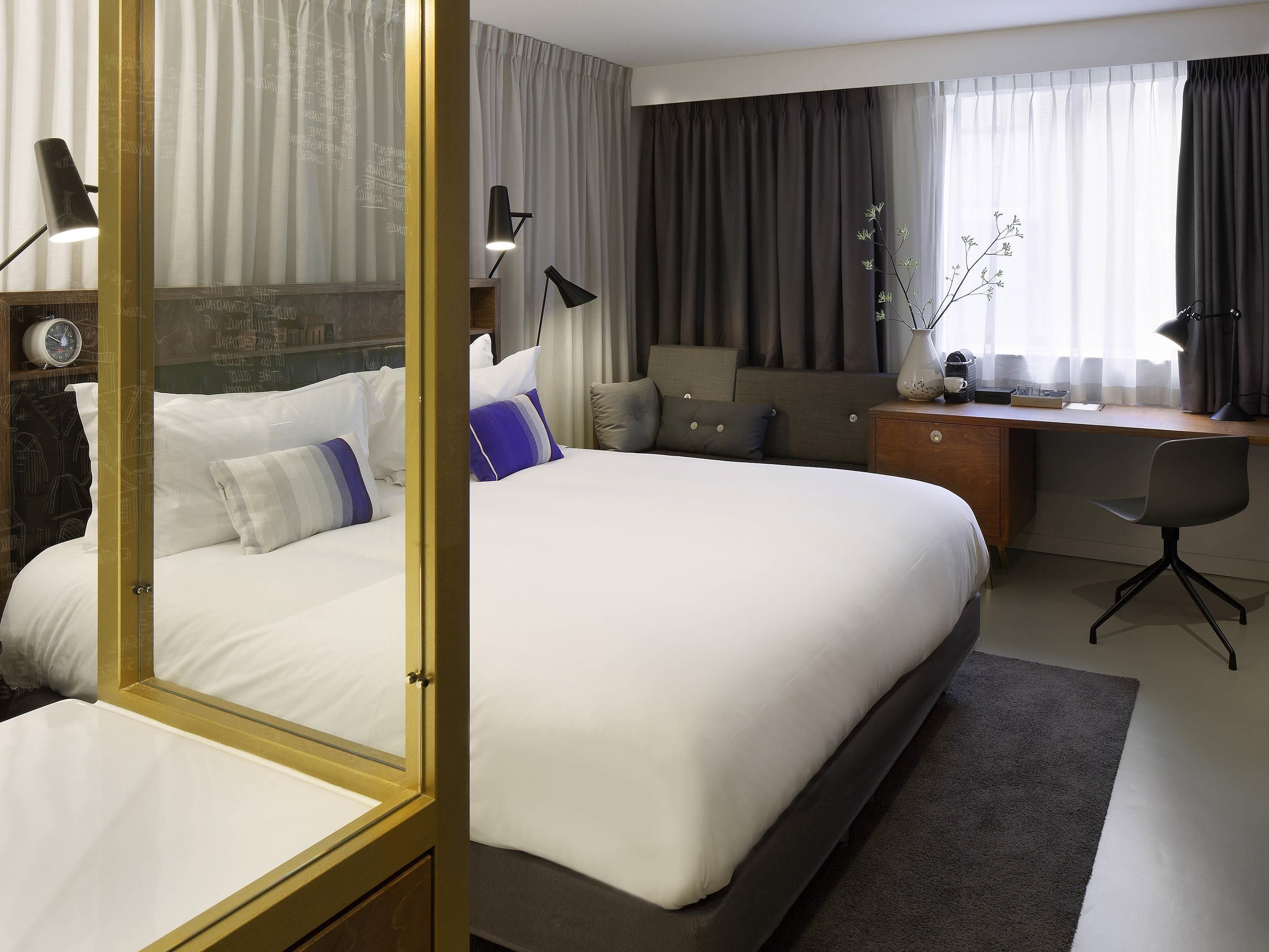 A hotel room with a large bed, a desk, a chair, and a nightstand.