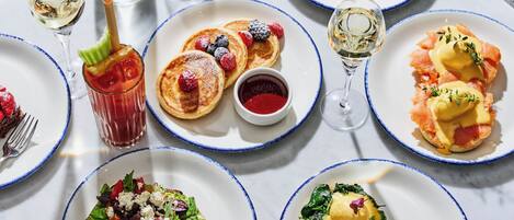 A table set with various breakfast dishes, including pancakes, eggs benedict, and a salad.