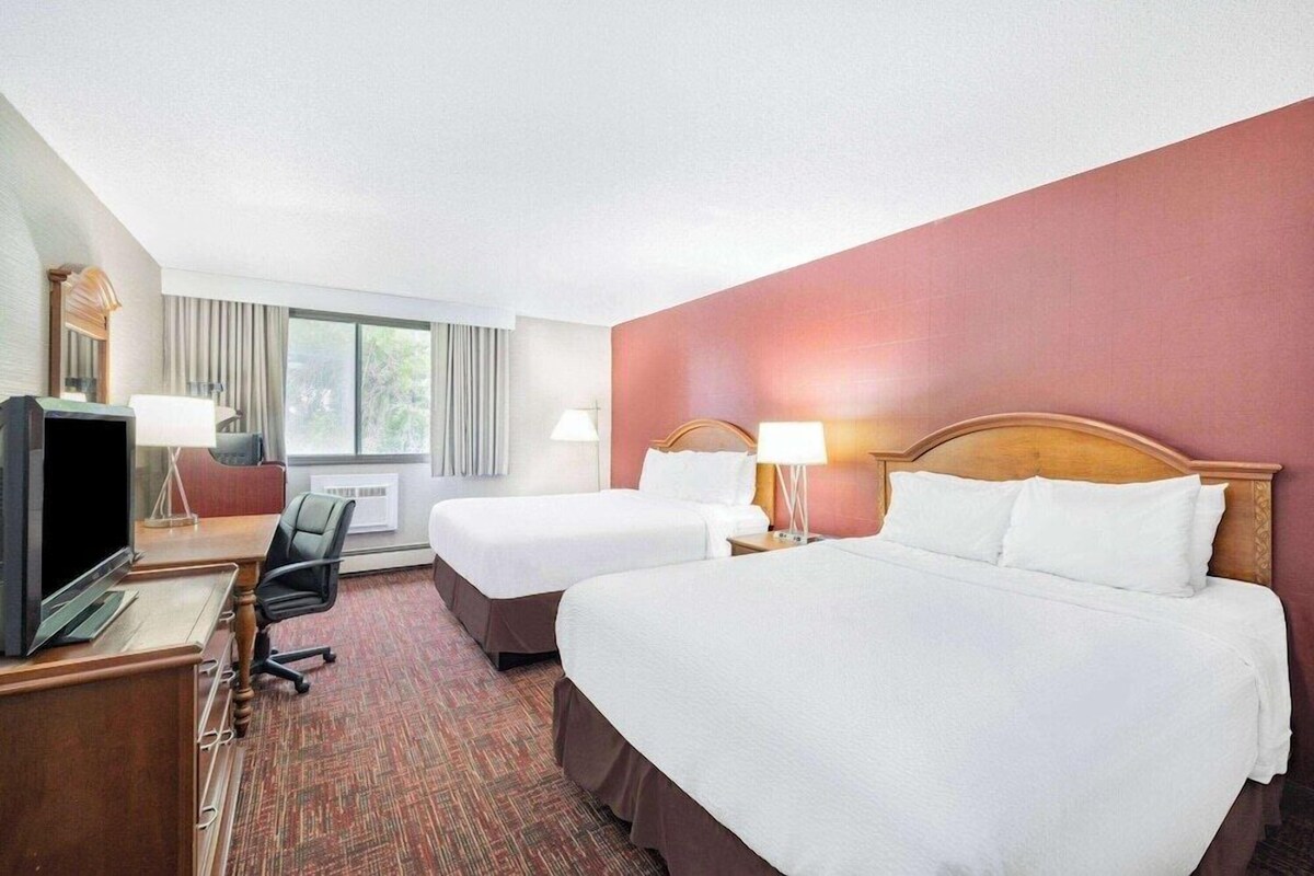 A hotel room with two single beds, a double bed, a desk with a television, and a chair.