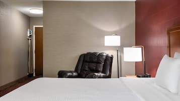 A hotel room with a large bed, a leather chair, a nightstand with a lamp, and a wall-mounted heater.
