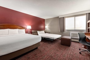A hotel room with a large bed, a smaller bed, a desk, a chair, a lamp, and a window with curtains.
