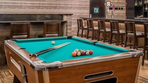 A pool table with a wooden frame and a green felt surface, surrounded by wooden chairs. - Ramada by Wyndham Grand Forks (Grand Forks)