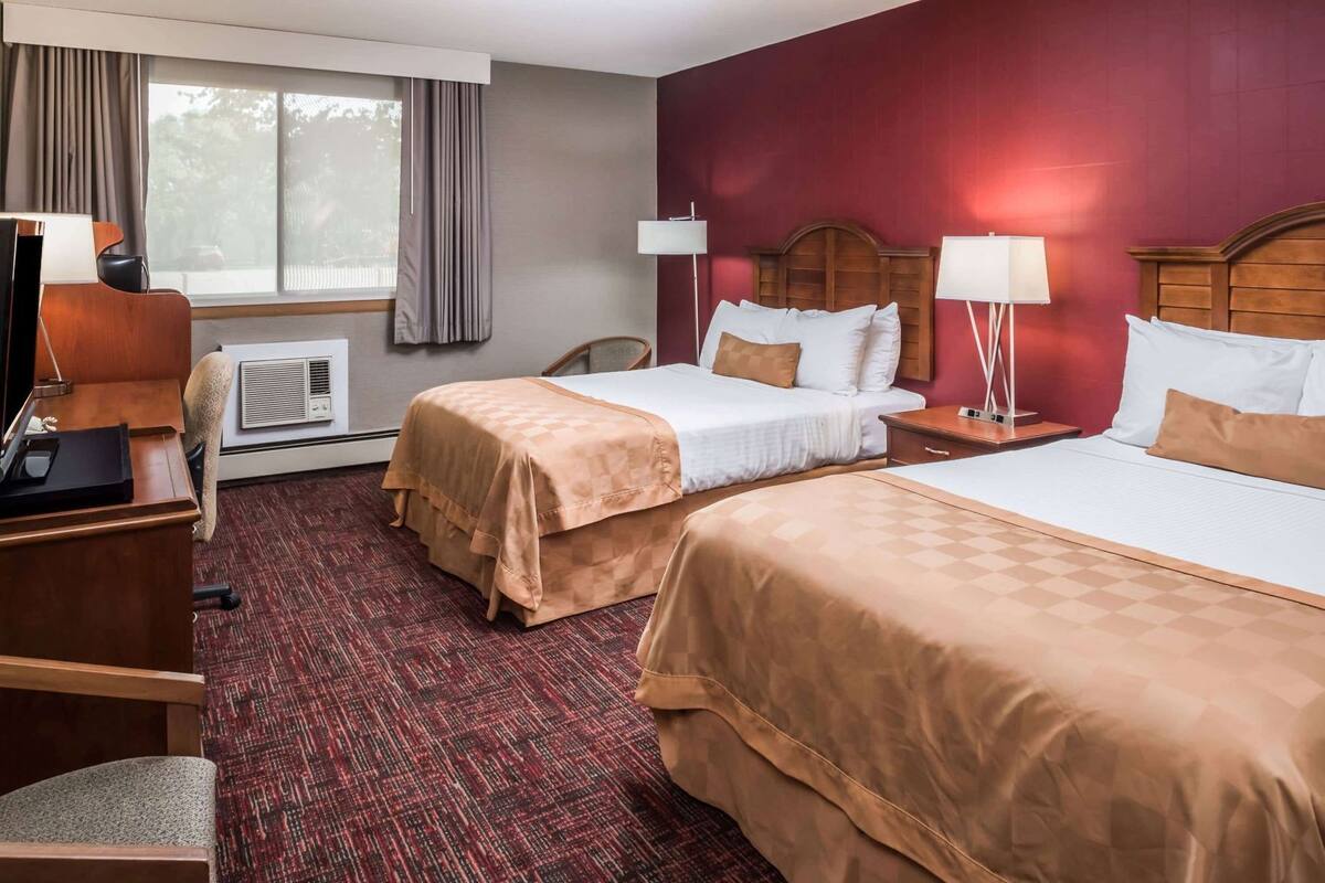 A hotel room with two beds, a desk, a chair, a TV, and a window with curtains.