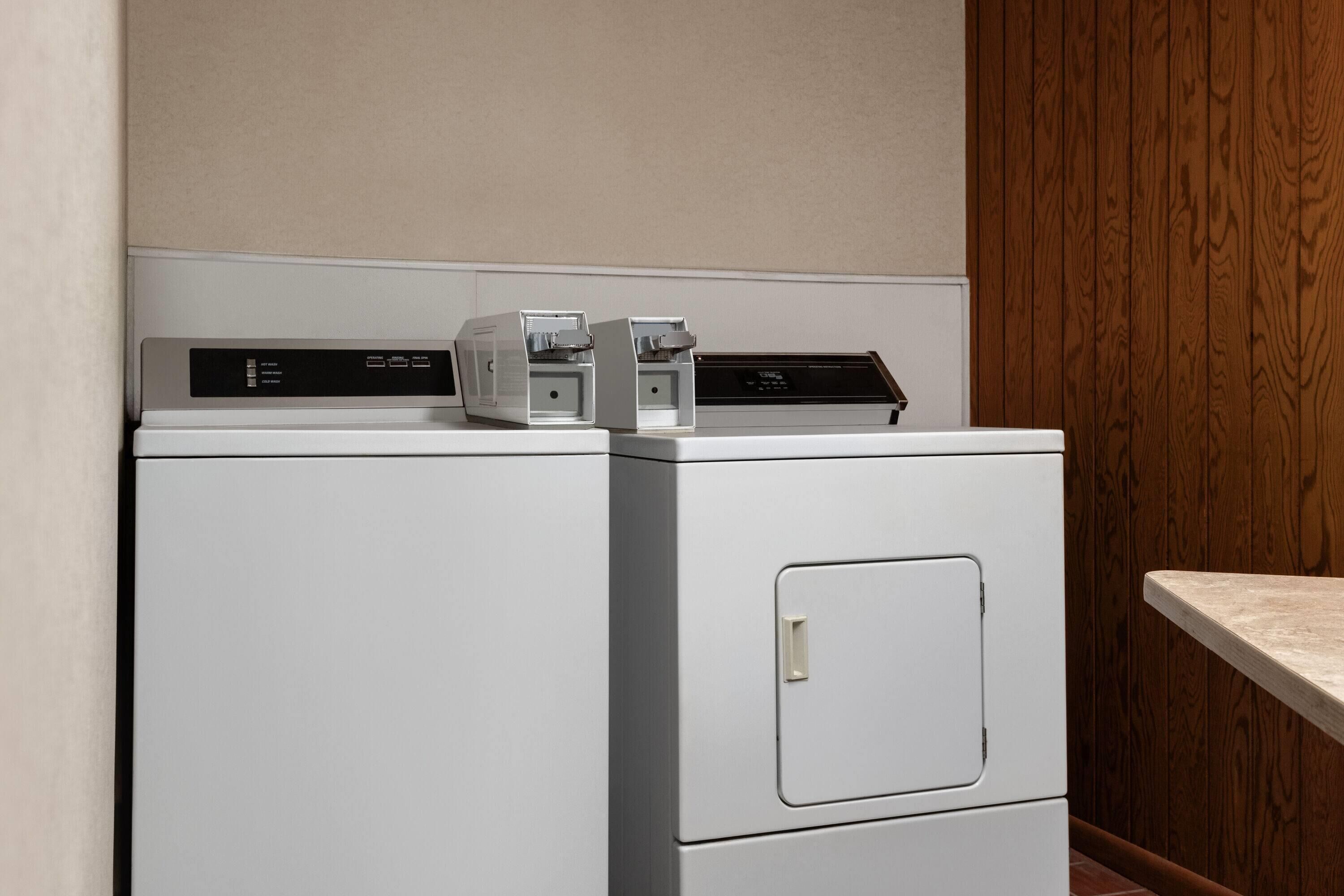 A laundry room with stacked washers and dryers, a wooden wall, and a countertop.