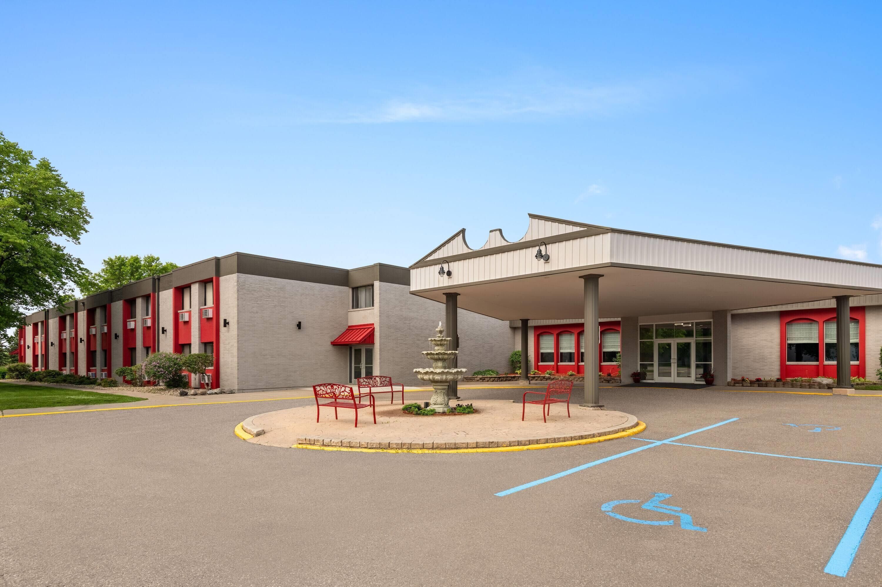 A building with a covered entrance, a parking lot with marked handicapped spaces, and a fountain.