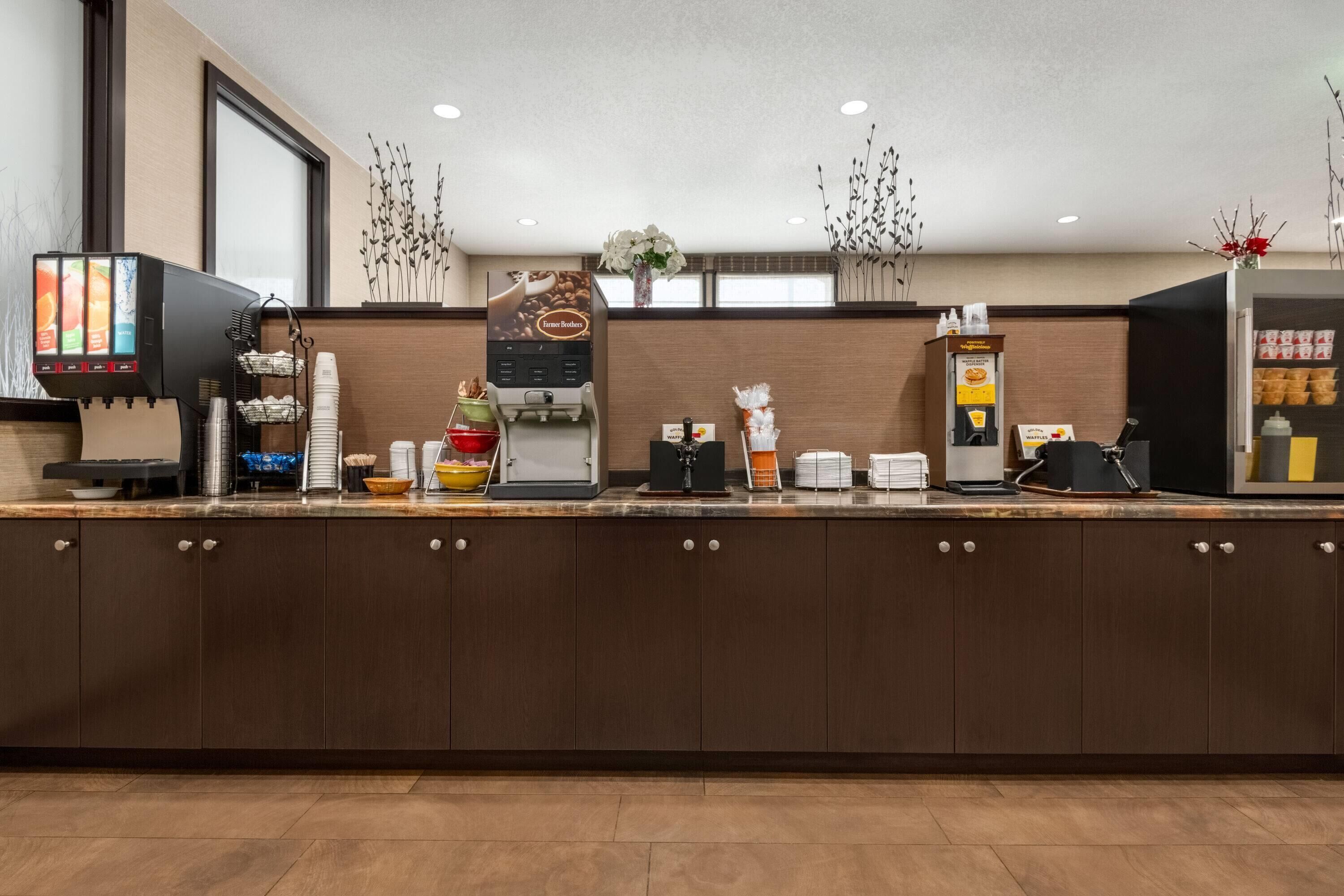 A hotel reception area with a coffee machine, a digital screen, and a menu board.