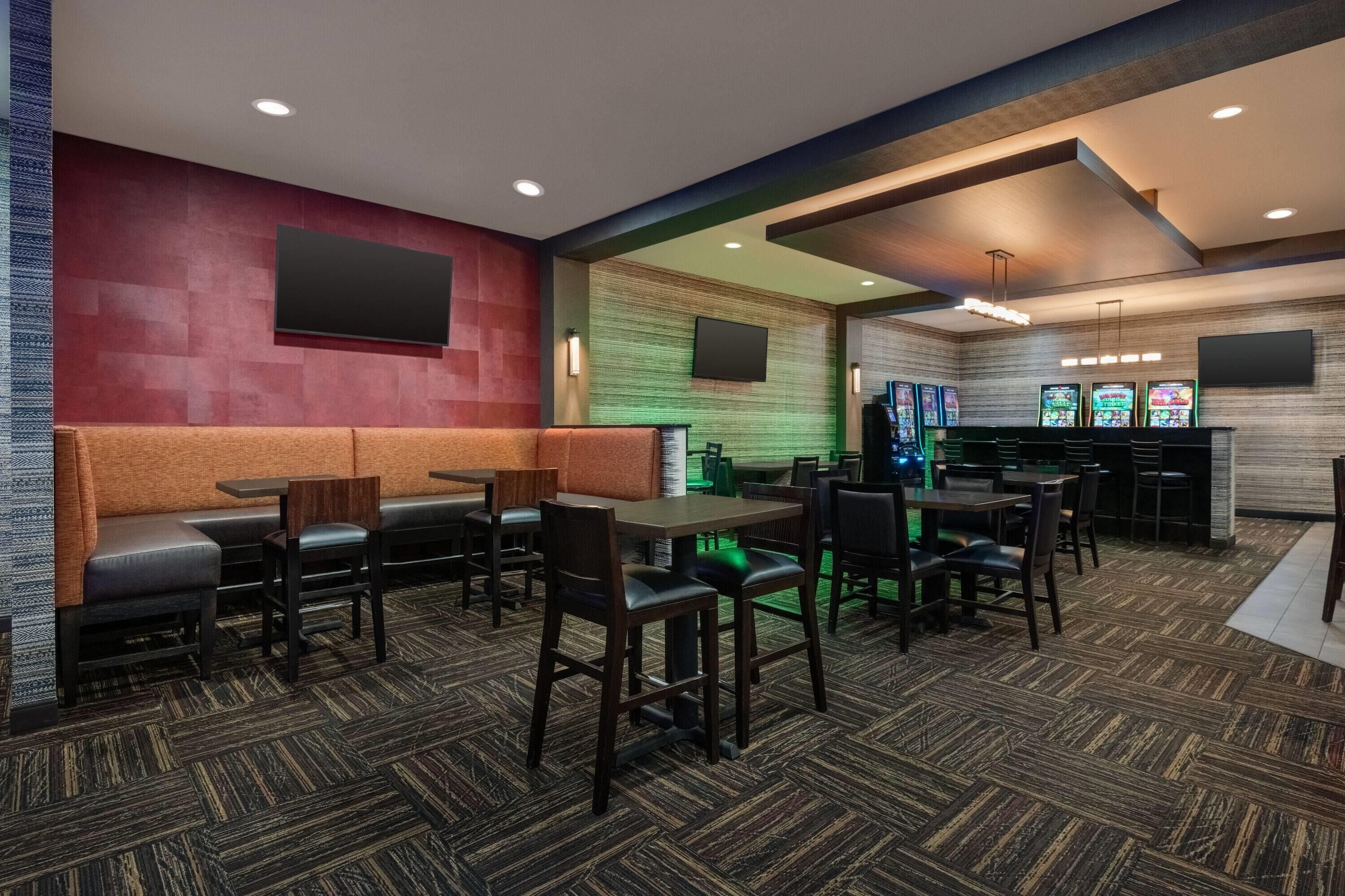 A restaurant with booths and tables, a bar area with slot machines, and a green-lit wall.