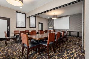 Un salón de conferencias con una mesa grande, sillas, una pantalla de proyector y una zona de presentaciones.